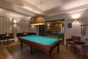 A pool table with a hanging light fixture, a billiards rack, and a seating area with chairs.