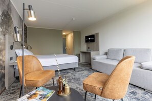 A hotel room with a bed, two armchairs, a coffee table, a TV, and a wall-mounted TV.