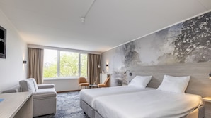Quarto de hotel com uma cama grande, uma escrivaninha, uma cadeira e vista para o exterior.