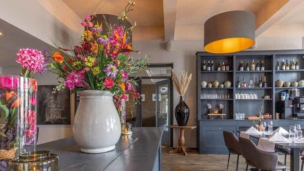 Een moderne barruimte met een grote bloemenvaas, een wijnrek en een eettafel met stoelen.