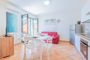 A compact kitchen with a dining area, a red sofa, and a large window. - Affittimoderni Valledoria - La Duna Bianca (Valledoria)
