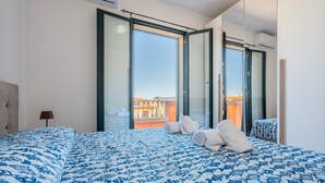 Ein Schlafzimmer mit einem großen Bett, Blick durch eine Schiebetür und ein Balkon mit Geländer.