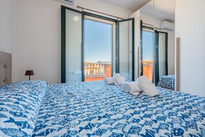 A bedroom with a large bed, a view through a sliding door, and a balcony with a railing. - Affittimoderni Valledoria - La Duna Bianca (Valledoria)