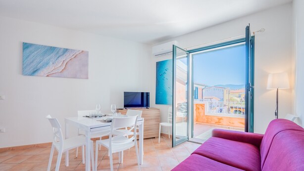 Ein modernes Wohnzimmer mit einem roten Sofa, einem Essbereich mit weißen Stühlen, einem Fernseher und einem Balkon mit Aussicht.