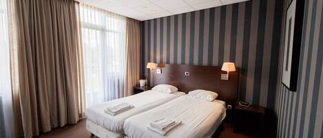 A hotel room with a large bed, two bedside tables, a headboard, and a window with curtains.
