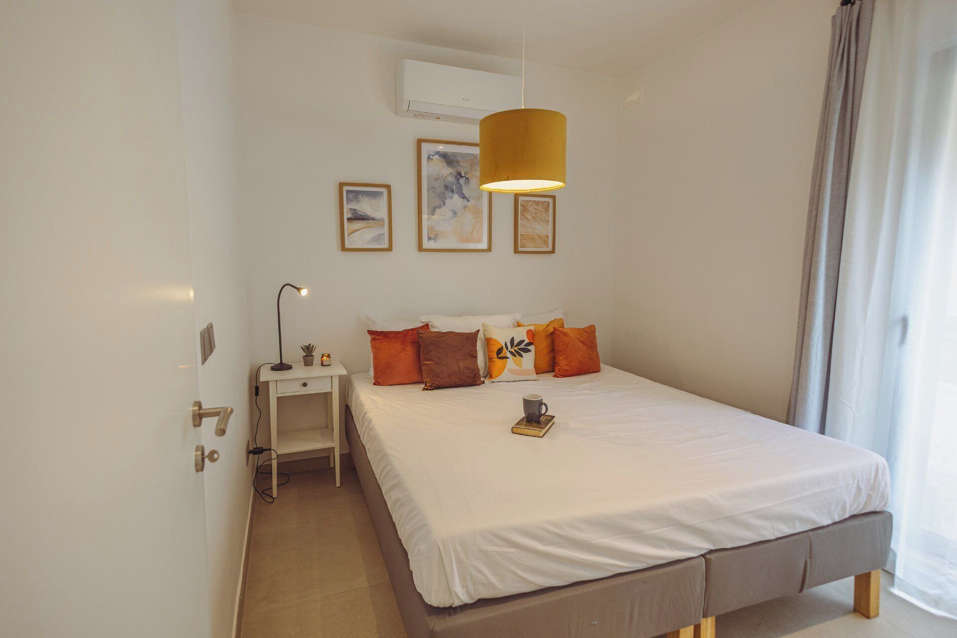 A bedroom with a bed, bedside table, lamp, and wall art.