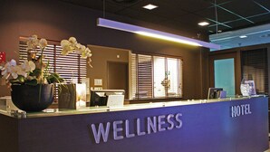 Ein Hotelrezeptionstresen mit einem 'WELLNESS'-Schild, einem Blumentopf und einer Rezeptionstheke.