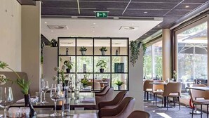 Ravintola, jossa on ruokailuun katetut pöydät, hylly, jossa on kirjoja ja kasveja, sekä näkymä suurista ikkunoista.