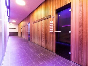 Un pasillo con paneles de madera, suelo de baldosas y una puerta que da a un interior iluminado de morado.