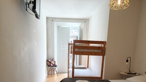 Una habitació amb un llit superposat, un escriptori amb una làmpada, una cadira i una làmpada penjant.