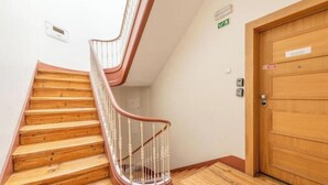 Una escala de fusta amb barana blanca, una porta de fusta amb un senyal i una làmpada de paret.