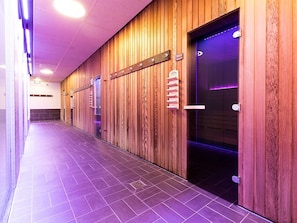 Un couloir aux murs lambrés, doté d’un sol carrelé et d’une porte dont l’intérieur est illuminé d’une lumière violette.