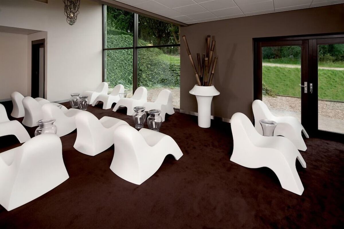 Una habitación con sillas blancas dispuestas alrededor de una mesa, ventanas amplias y vistas a zonas verdes.
