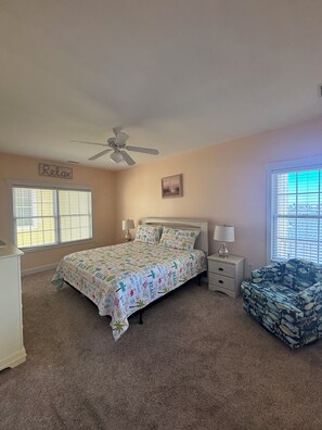 A bedroom with a bed, a nightstand, a chair, a ceiling fan, and a window with blinds.