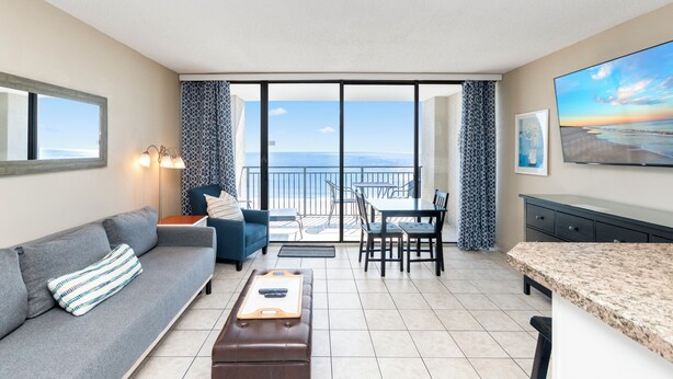 Ein modernes Wohnzimmer mit Sofa, Couchtisch, Esstisch mit Stühlen, Küchenzeile und Balkon mit Meerblick.