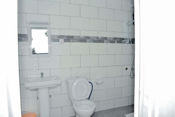 A bathroom with white tiles, a sink, a toilet, and a shower. - Inzozi Africa House B&B (Kigali)