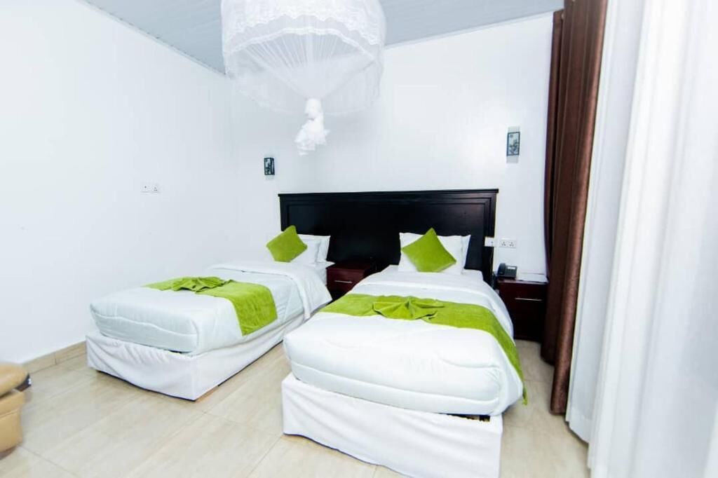 A hotel room with two beds, a dark headboard, a nightstand, and a hanging light fixture.