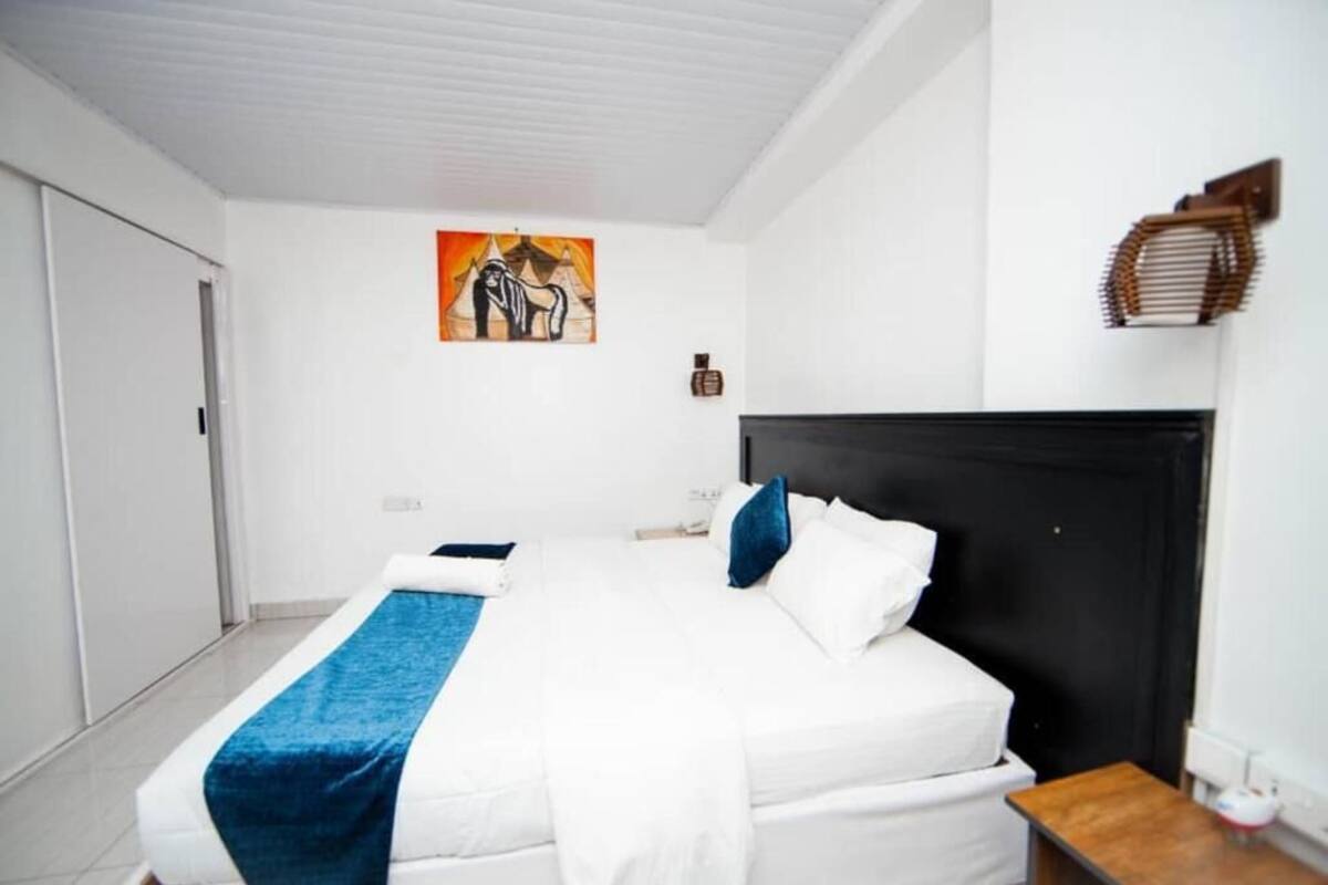 A bedroom with a bed, a nightstand, a wall-mounted lamp, and a painting.