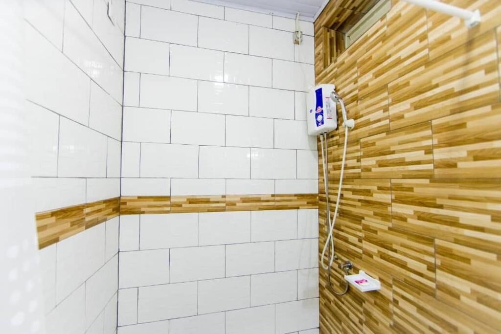 Une salle de bain avec des murs recouverts de carreaux blancs, un mur d’accent en bois et une prise électrique visible.