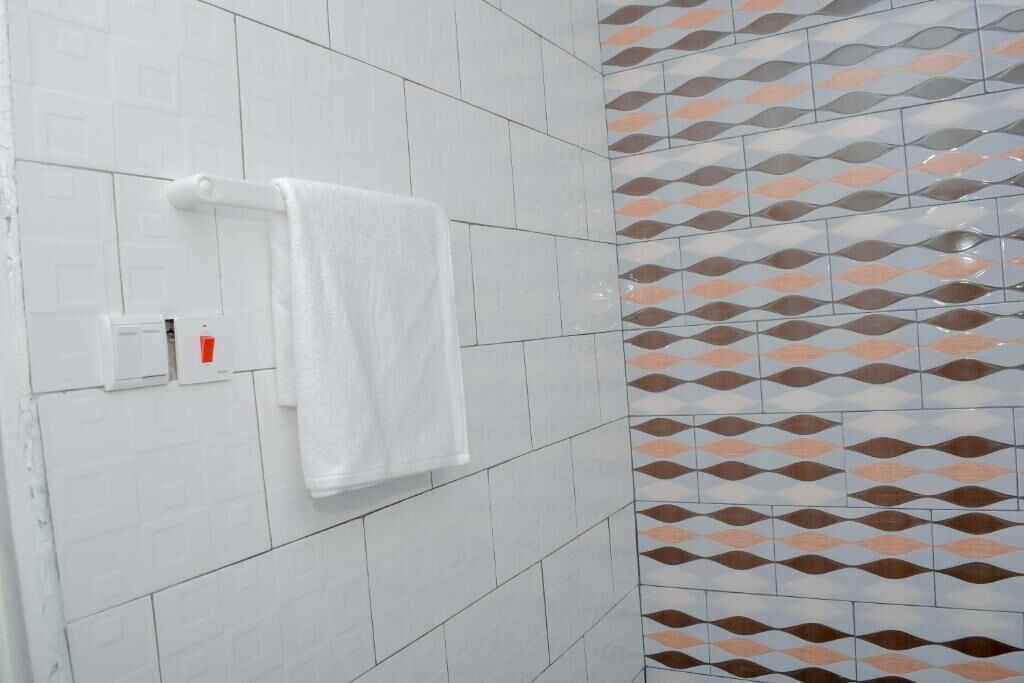 A bathroom with white tiles, a towel rack, and patterned tiles on the wall.