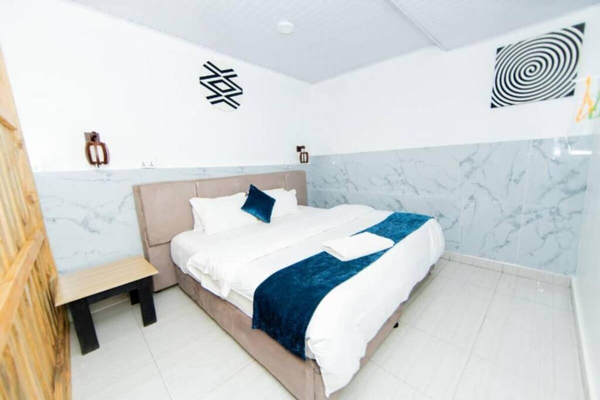 A modern hotel room with a bed, a small wooden stool, and a wall with a circular design.