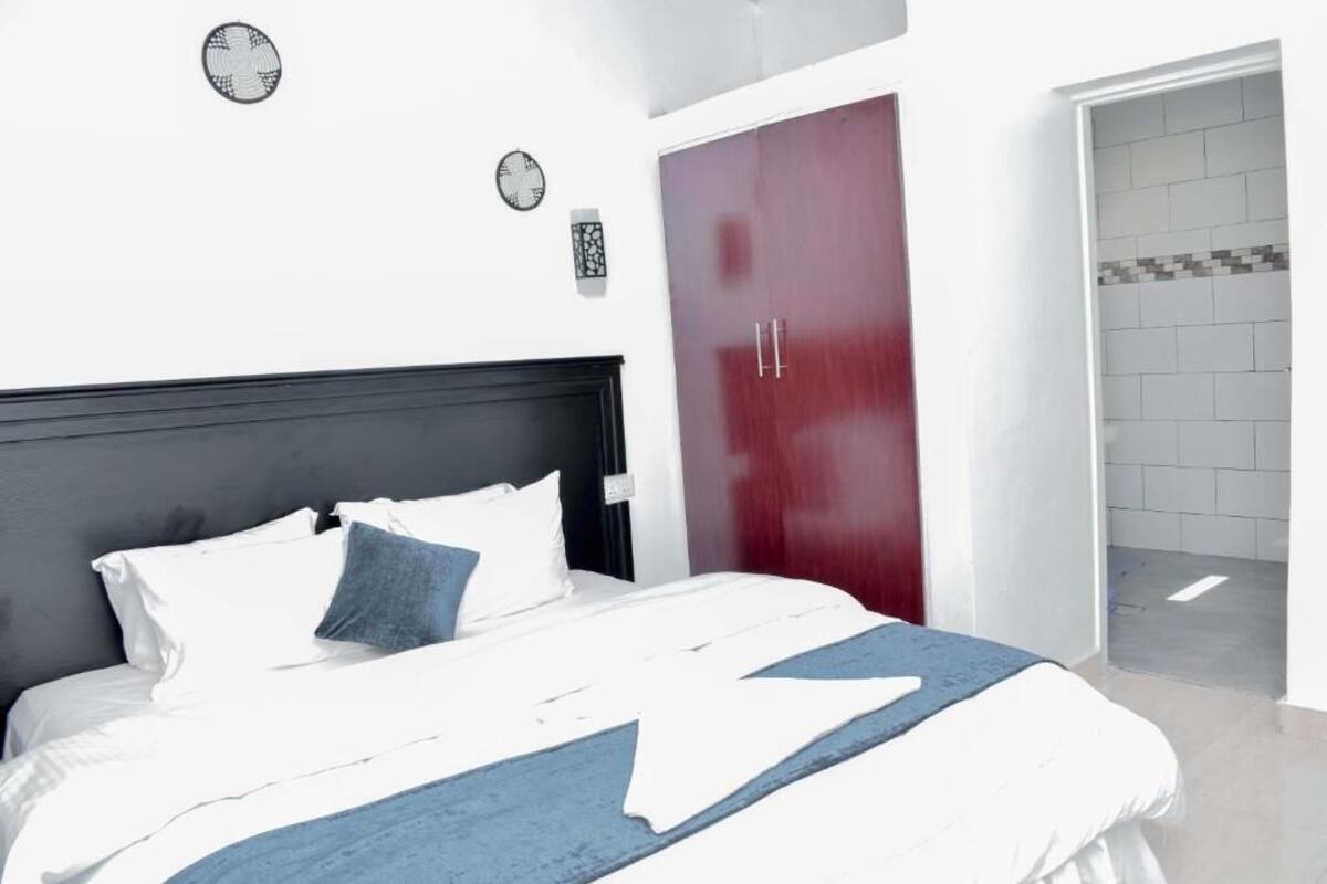 A bedroom with a bed, a red wardrobe, and a white wall with a clock.