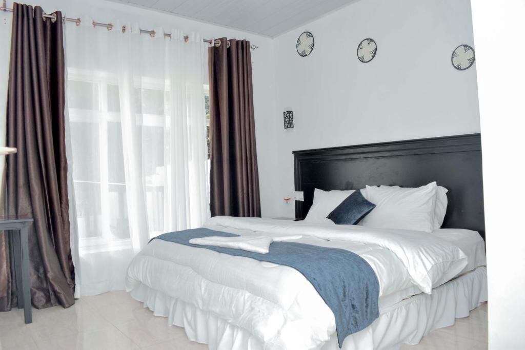 A bedroom with a large bed, curtains, a bedside table, and a wall clock.