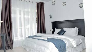 A bedroom with a large bed, curtains, a bedside table, and a wall clock.