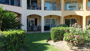 A multi-story building with balconies, a courtyard with grass and bushes, and a flag.