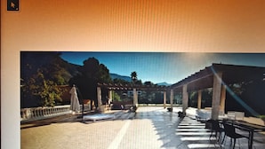 A covered outdoor area with a pergola, seating, and a view of a mountainous landscape.