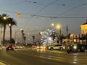 A street scene with a Ferris wheel, palm trees, and vehicles. - Audrey Beachside 2BR apartment, F1, Private Yard, free secure Parking (St Kilda)