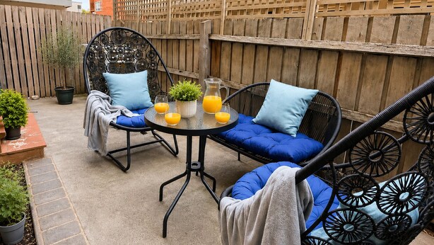 A patio with a round table, two chairs, and a sofa. There are potted plants and a wooden fence in the background. - Near St Kilda Beach Stay, Free Parking, Courtyard & Formula 1 (St Kilda)