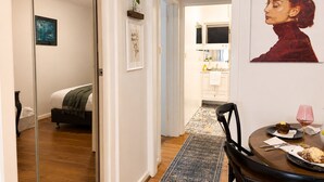 A modern apartment with a bed, a dining area with a table and chairs, a kitchen with a sink and cabinets, and a hallway leading to another room. - Near St Kilda Beach Stay, Free Parking, Courtyard & Formula 1 (St Kilda)