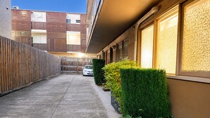 A narrow alleyway with a concrete path, a wooden fence, and a row of buildings with windows. - Near St Kilda Beach Stay, Free Parking, Courtyard & Formula 1 (St Kilda)