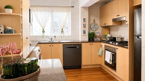 A modern kitchen with wooden cabinets, a dishwasher, an oven, and a stove. - Near St Kilda Beach Stay, Free Parking, Courtyard & Formula 1 (St Kilda)