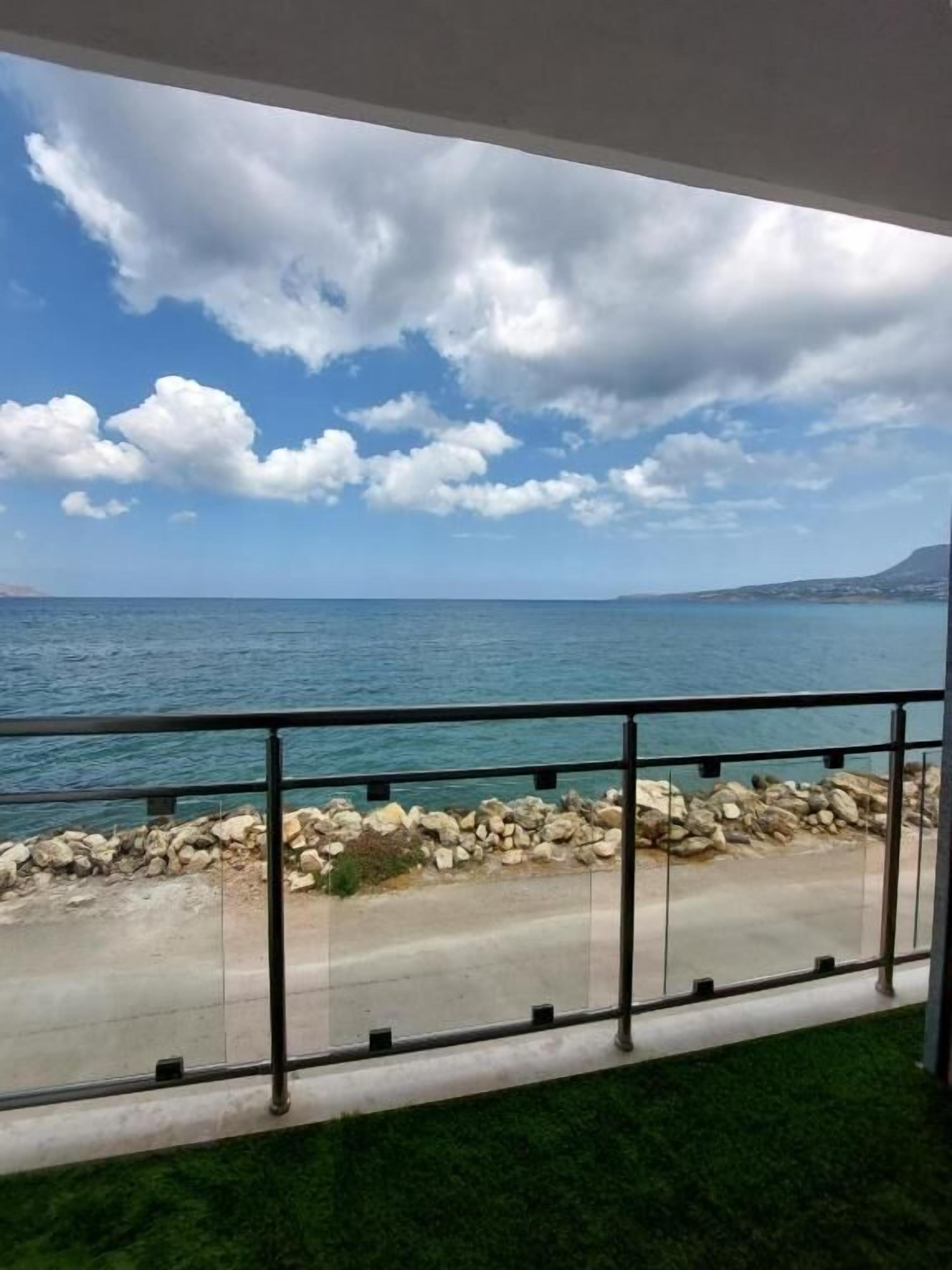 A balcony with a view of the sea, a stone wall, and a grassy area.