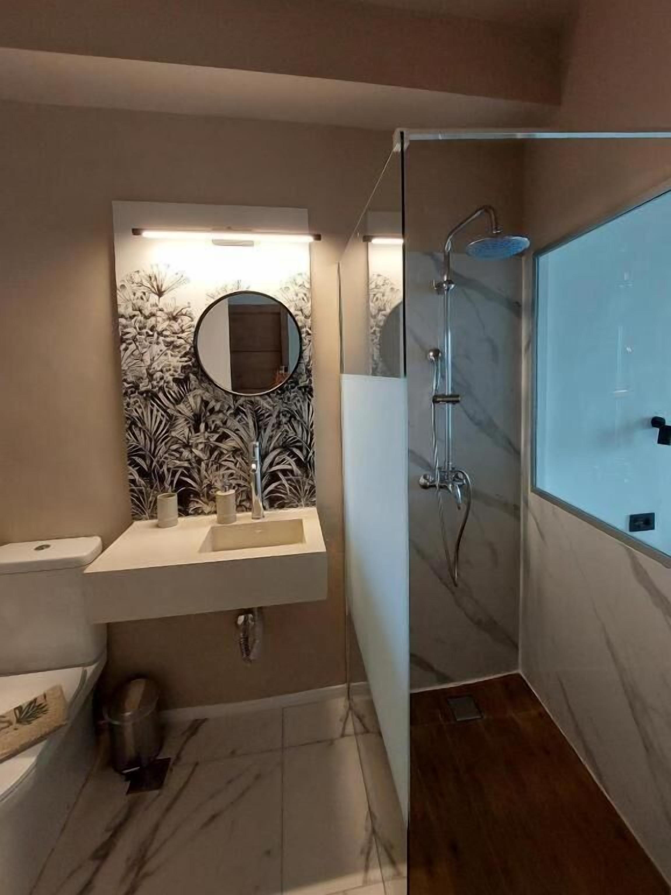 A bathroom with a marble sink, a toilet, a shower with a glass door, and a wall-mounted mirror.