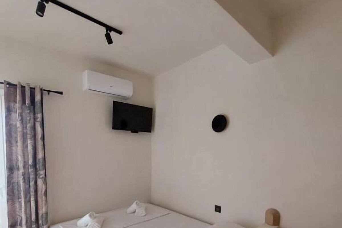 A single bed with a headboard, a flat-screen TV mounted on the wall, and a ceiling-mounted light fixture.