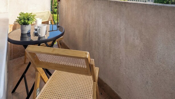 Ein Balkon mit Tisch und Stühlen, einem Blumentopf und Blick auf Gebäude im Hintergrund.