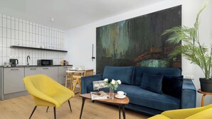 Ein zeitgemäßer Wohnraum mit einer Couch, gelben Sesseln, einem Couchtisch, einem großen abstrakten Gemälde und einer Küchenzeile.