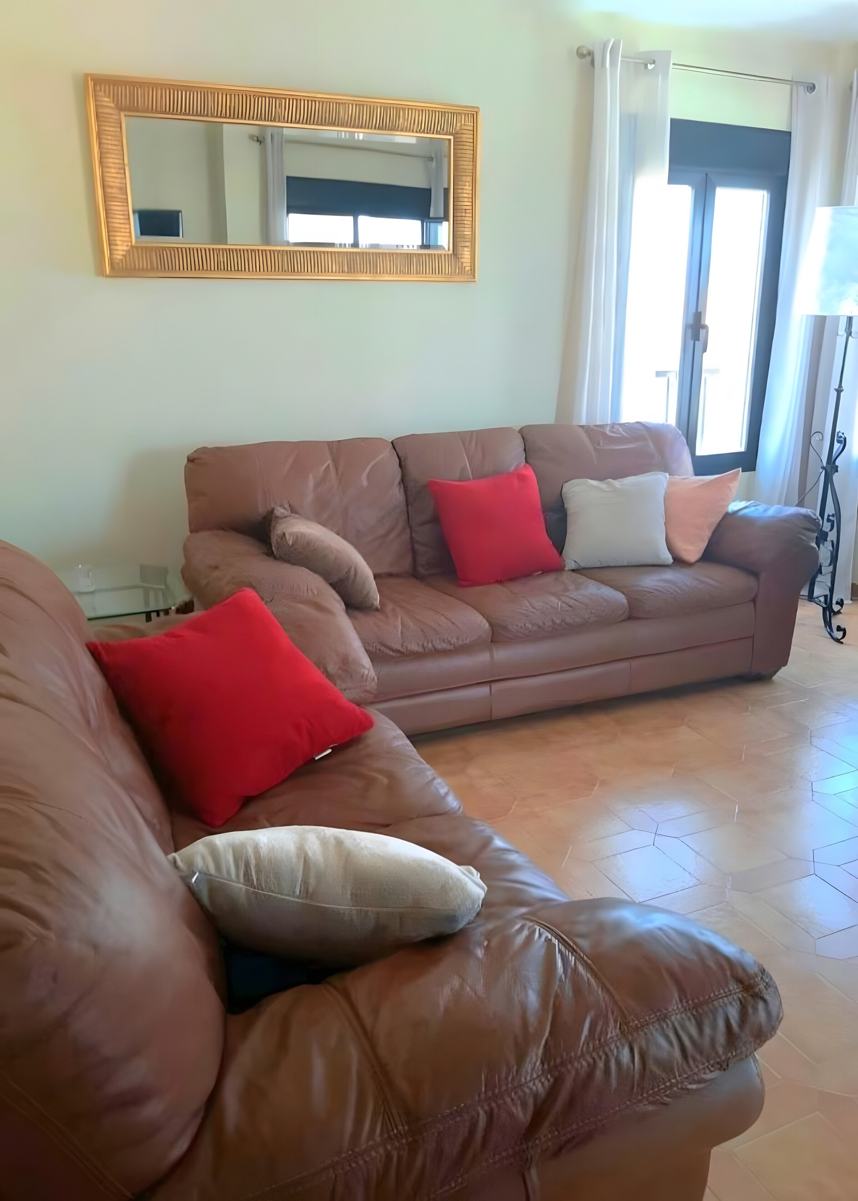 A living room with a brown leather sofa, a large mirror, and a floor lamp.