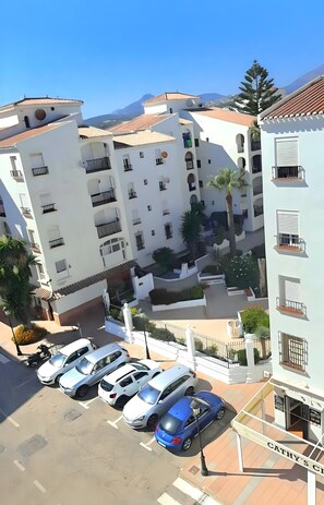 A multi-story residential building with balconies, a parking area with several cars, and a clear view of the surrounding landscape.