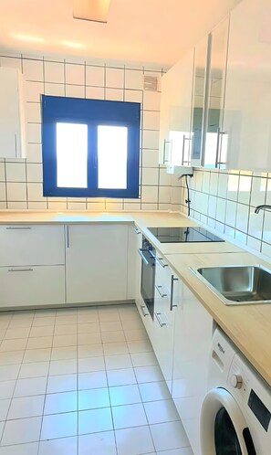 Eine moderne Küche mit weißen Schränken, einem Backofen, einem Geschirrspüler, einer Spüle und einem Fenster.
