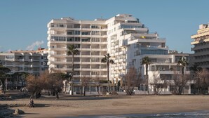 Un edificio costero con varios balcones, una playa de arena y palmeras.