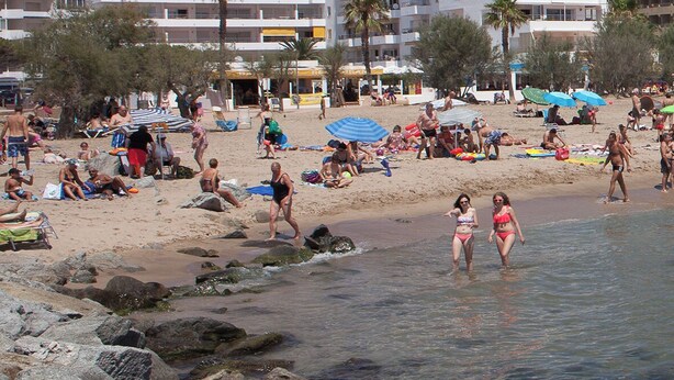 Una playa con gente, un edificio con varios balcones y un cielo despejado.