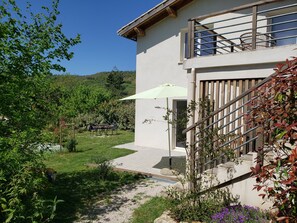 Une maison dotée d’un balcon, d’un espace extérieur aménagé et couvert, et d’un chemin de gravier menant à l’entrée.