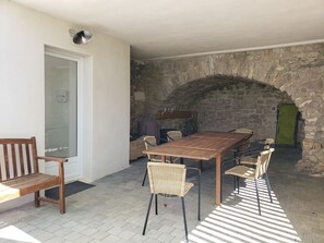 Une terrasse avec une table en bois et des chaises en osier, un mur en pierre et une porte.