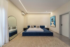 Un dormitorio moderno con una cama grande, un espejo, aire acondicionado, una mesita de noche, una lámpara y un cuadro.