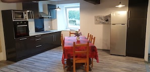 Cocina compacta con horno integrado, microondas y refrigerador, una mesa de comedor con sillas y un ventanal que proporciona luz natural.
