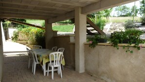 An outdoor patio with a table and chairs, a brick floor, and a covered area with a view of greenery. - Gîte de la Verdurette: Tranquil Stay in the Countryside (Pettonville)